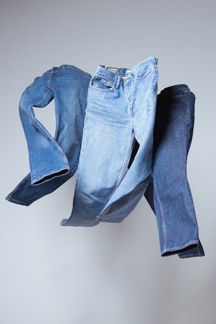 Three pairs of denim jeans in varying shades showcased against a gray backdrop, capturing different styles.