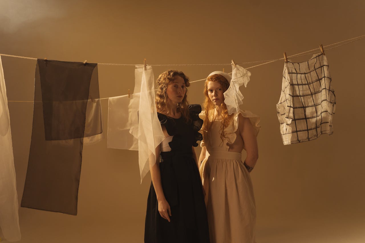 Two models pose in a studio with clothes hanging on a line, capturing an artistic fashion concept.