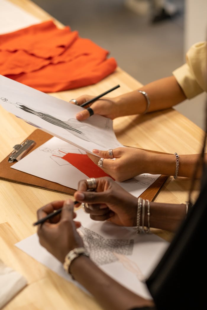 Fashion designers collaborating on sketches with vibrant red fabric inspiration in an indoor setting.